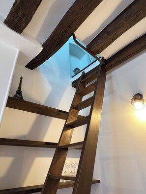 Eine Holzleiter führt zu einem Erkerbereich mit Oberlichter, einem kleinen Eiffelturm-Modell und einer Wandleuchte.