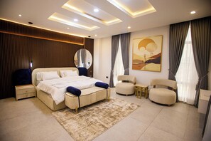 Un dormitorio moderno con una cama grande, mesitas de noche, un espejo, un sofá y una pequeña mesa.