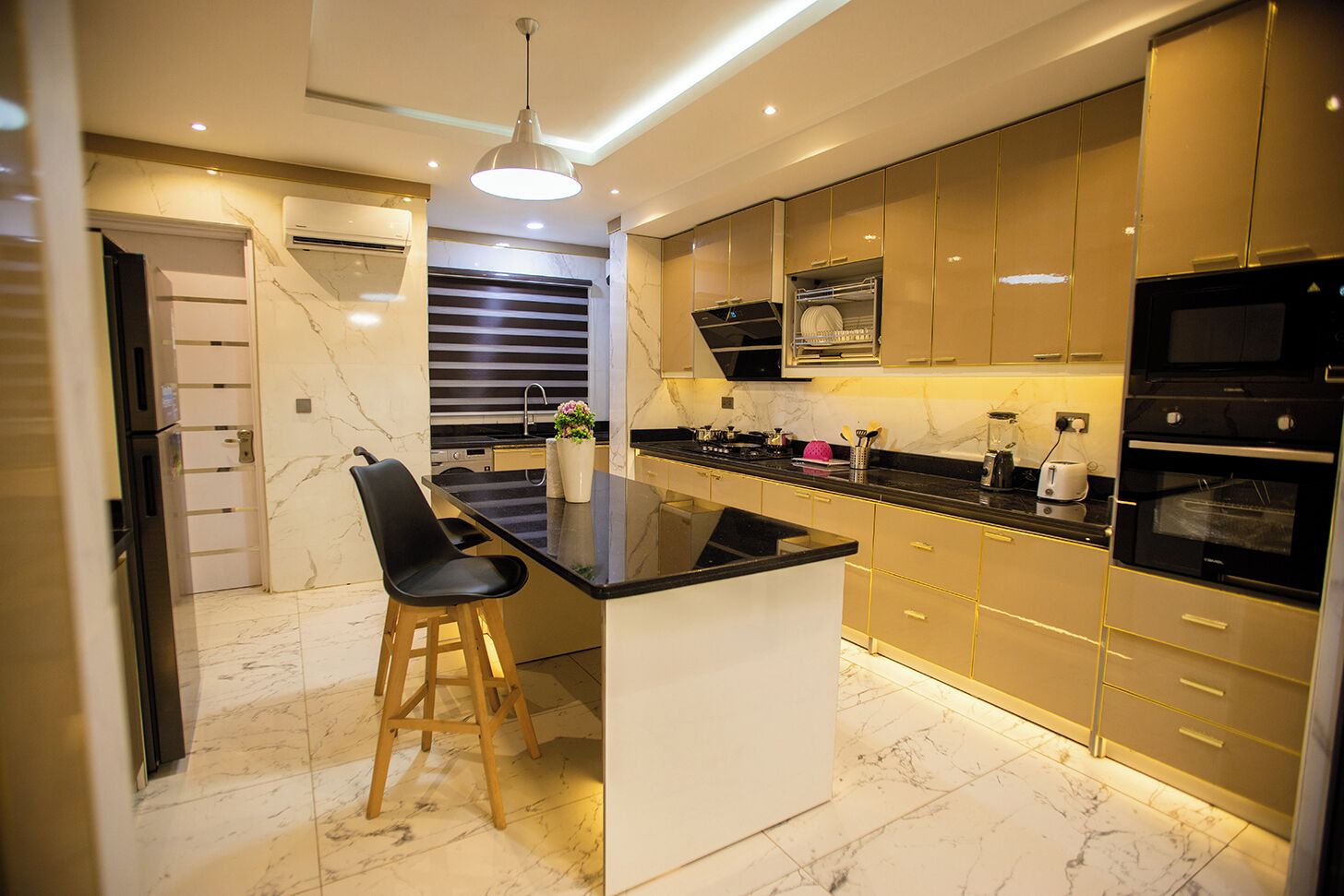 A modern kitchen with a central island, black bar stools, and gold-toned cabinets.