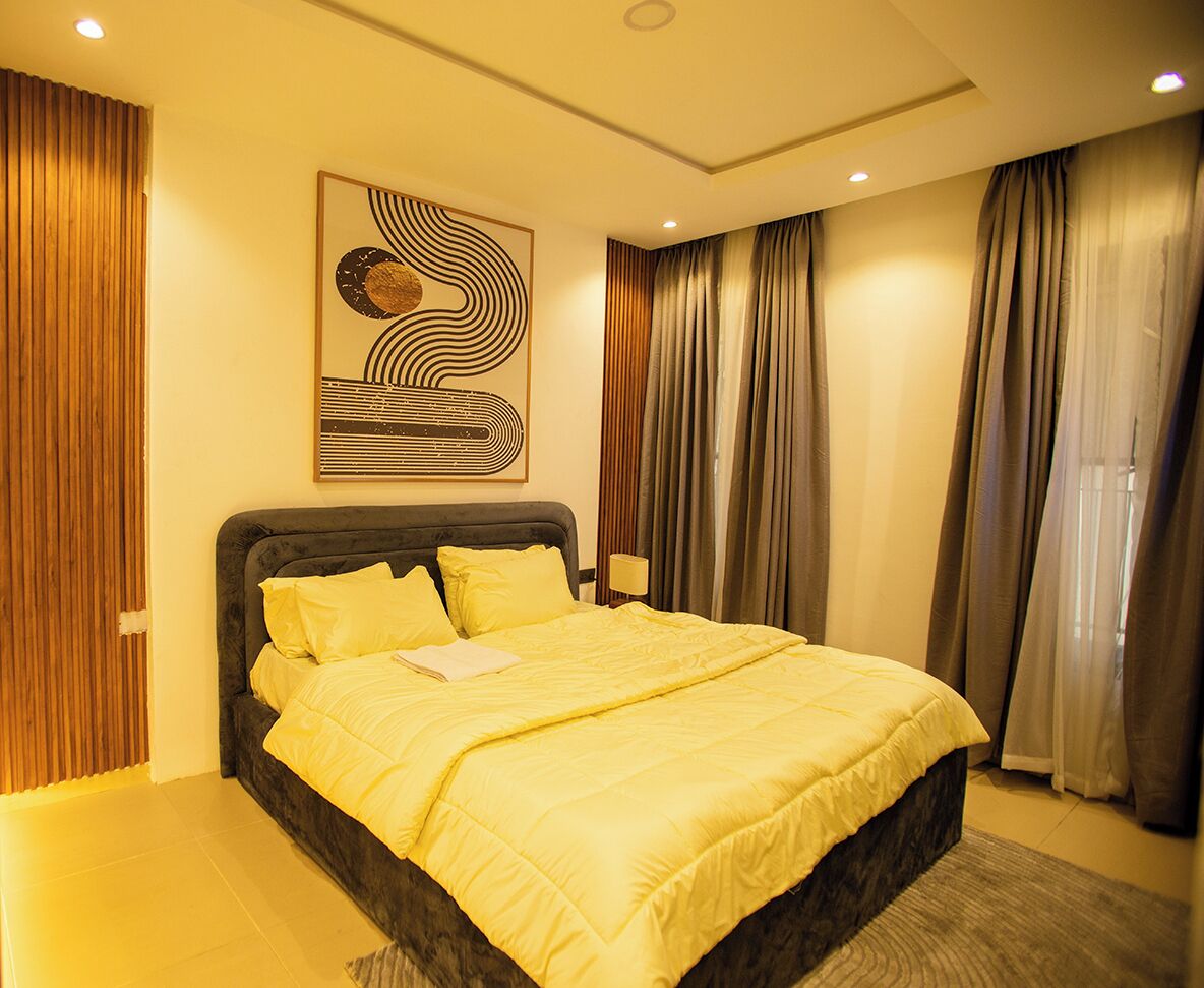 A modern bedroom with a large bed, a decorative wall piece, and curtains.