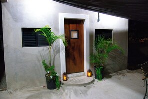 Entrada d'un edifici amb una porta de fusta, plantes en testos i fanals.
