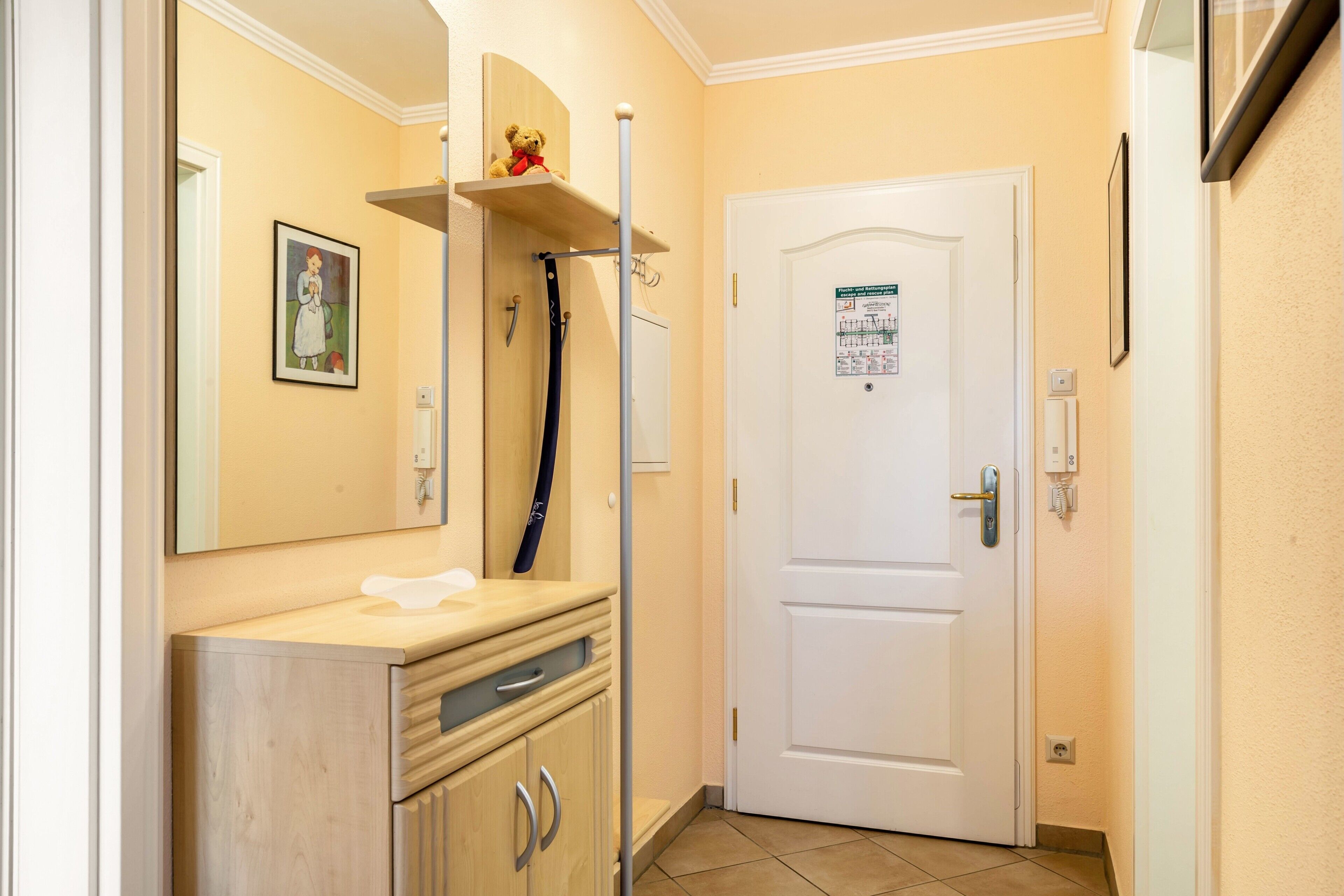 A bathroom with a mirror, a sink, a towel, a door with a sign, and a shelf with a teddy bear.