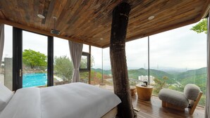 Un dormitorio con una cama grande, techo de madera, vista a una piscina y un tronco de árbol grande.