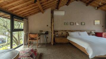 Ein Schlafzimmer mit Holzboden, einem Bett, einem Schreibtisch, einem Stuhl und einem Fenster mit Blick auf Bäume.