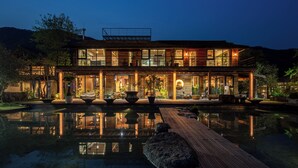 A modern house with a large glass facade, a wooden deck, and a reflective pool.