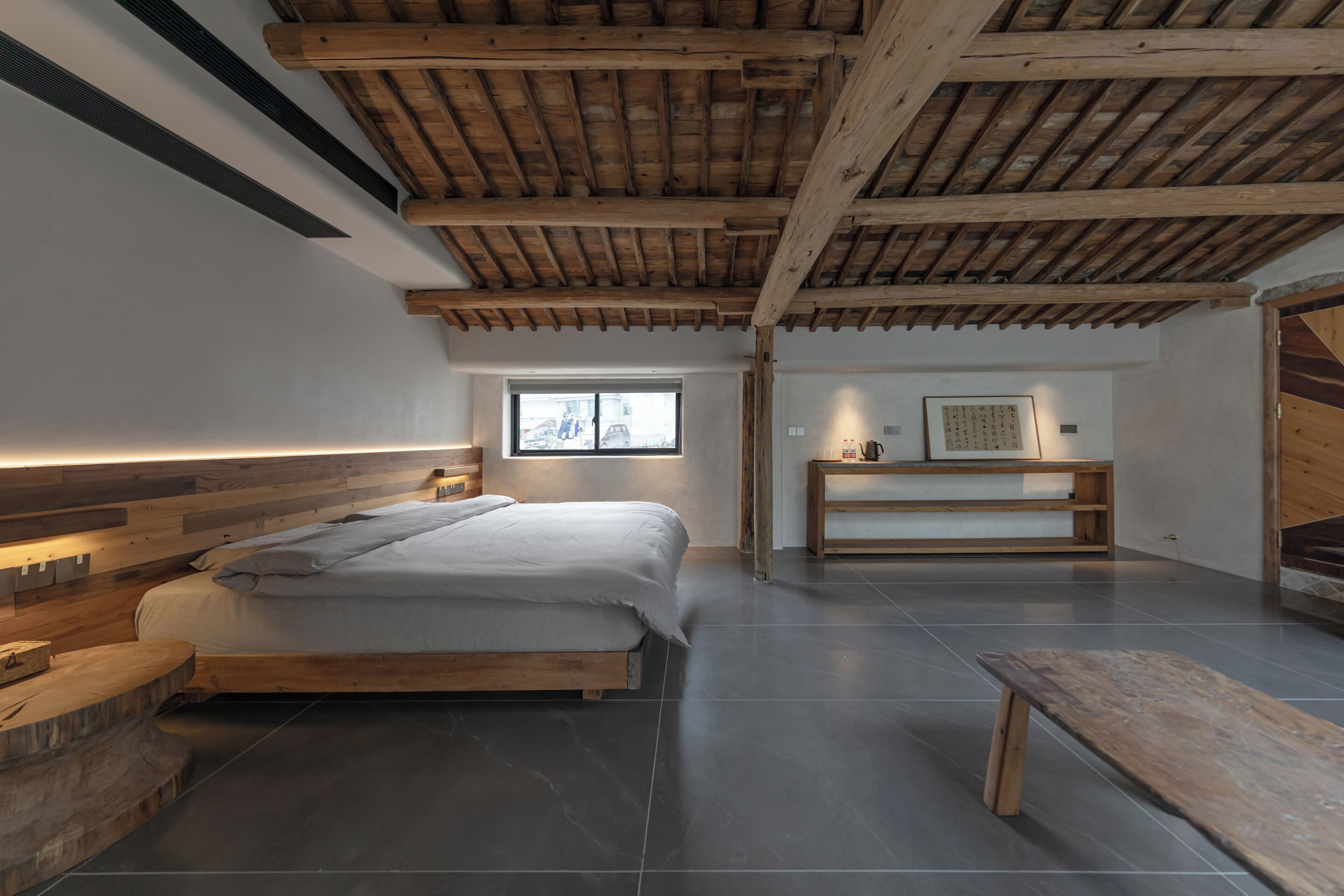 Un dormitorio con una cama de madera, un banco y una ventana.