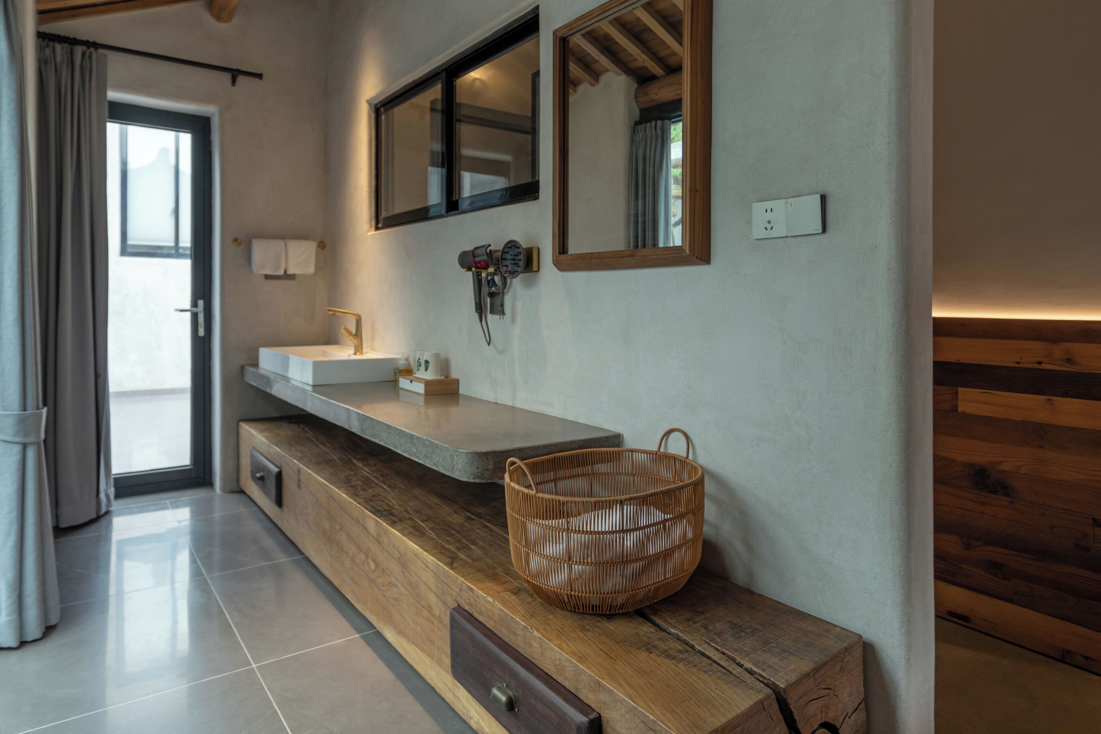 Un baño con tocador de madera, un espejo grande, perchero y cesta.