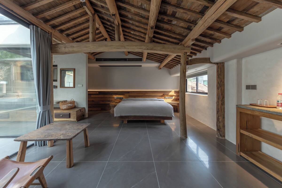 A bedroom with a wooden ceiling, a bed, a table, and a bench.