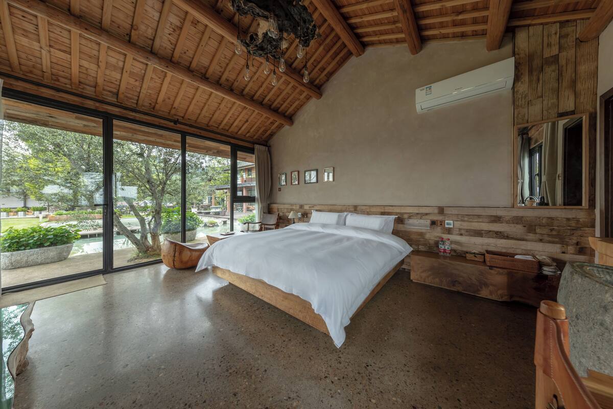 A bedroom with a large bed, wooden ceiling, and a view of the outdoors.