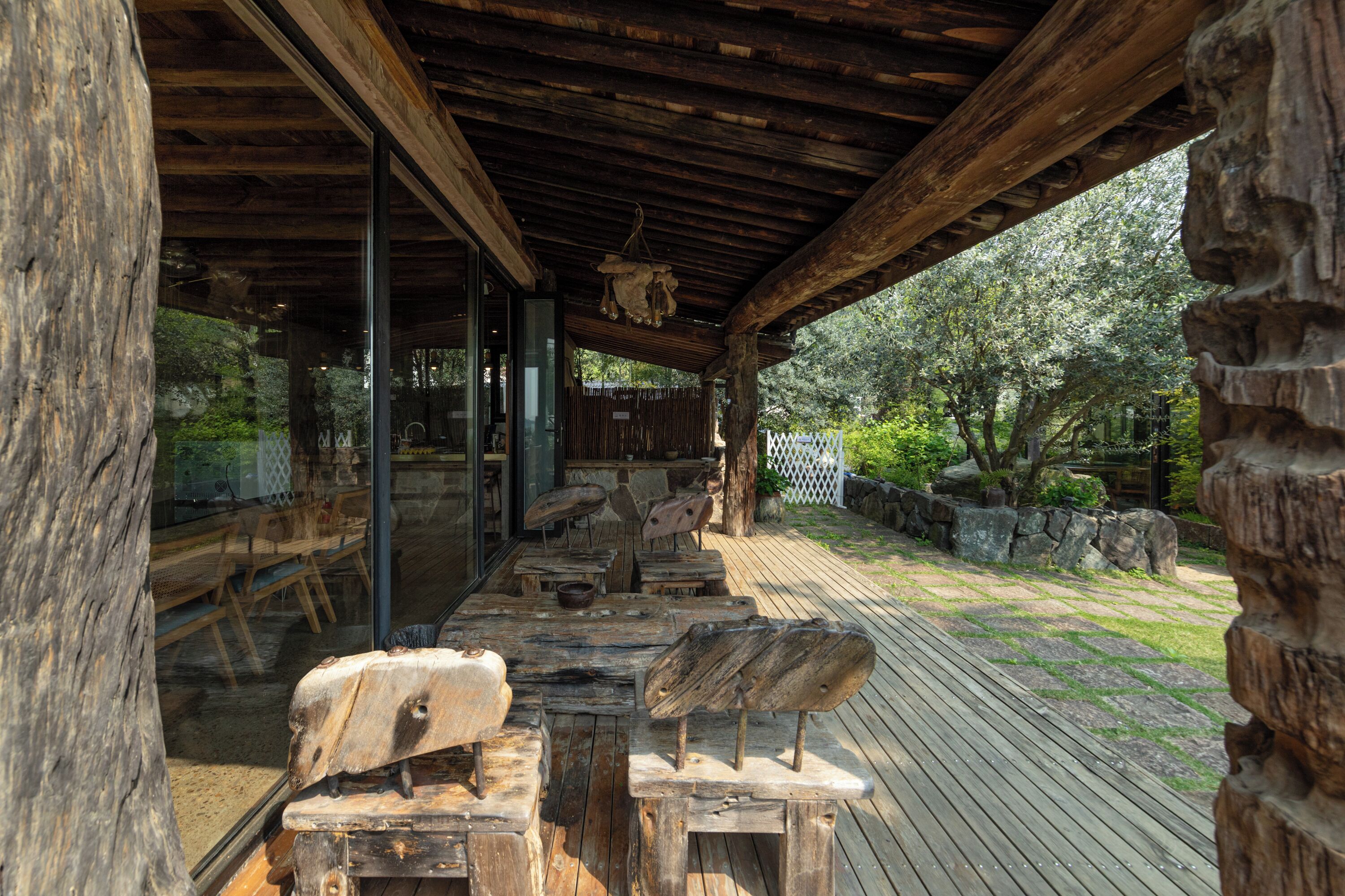 An outdoor wooden deck with rustic furniture, a glass enclosure, and a stone wall.