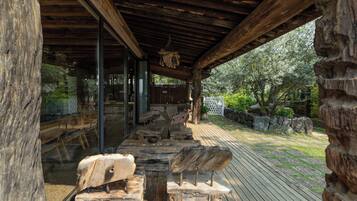 An outdoor wooden deck with rustic furniture, a glass enclosure, and a stone wall.
