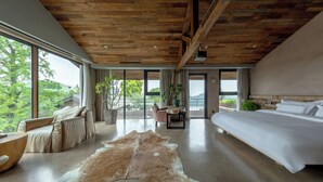 A spacious bedroom with a large bed, a leather sofa, a wooden ceiling, and a view of the outdoors.