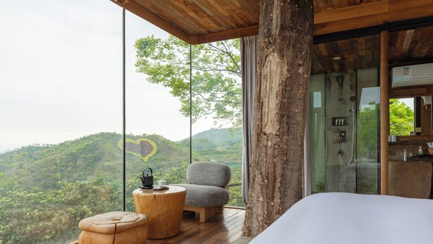 A bedroom with a large window, wooden flooring, a bed, a chair, and a small round table.