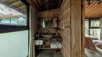 A rustic bathroom with a stone sink, wooden shelves, and a view of the outdoors.
