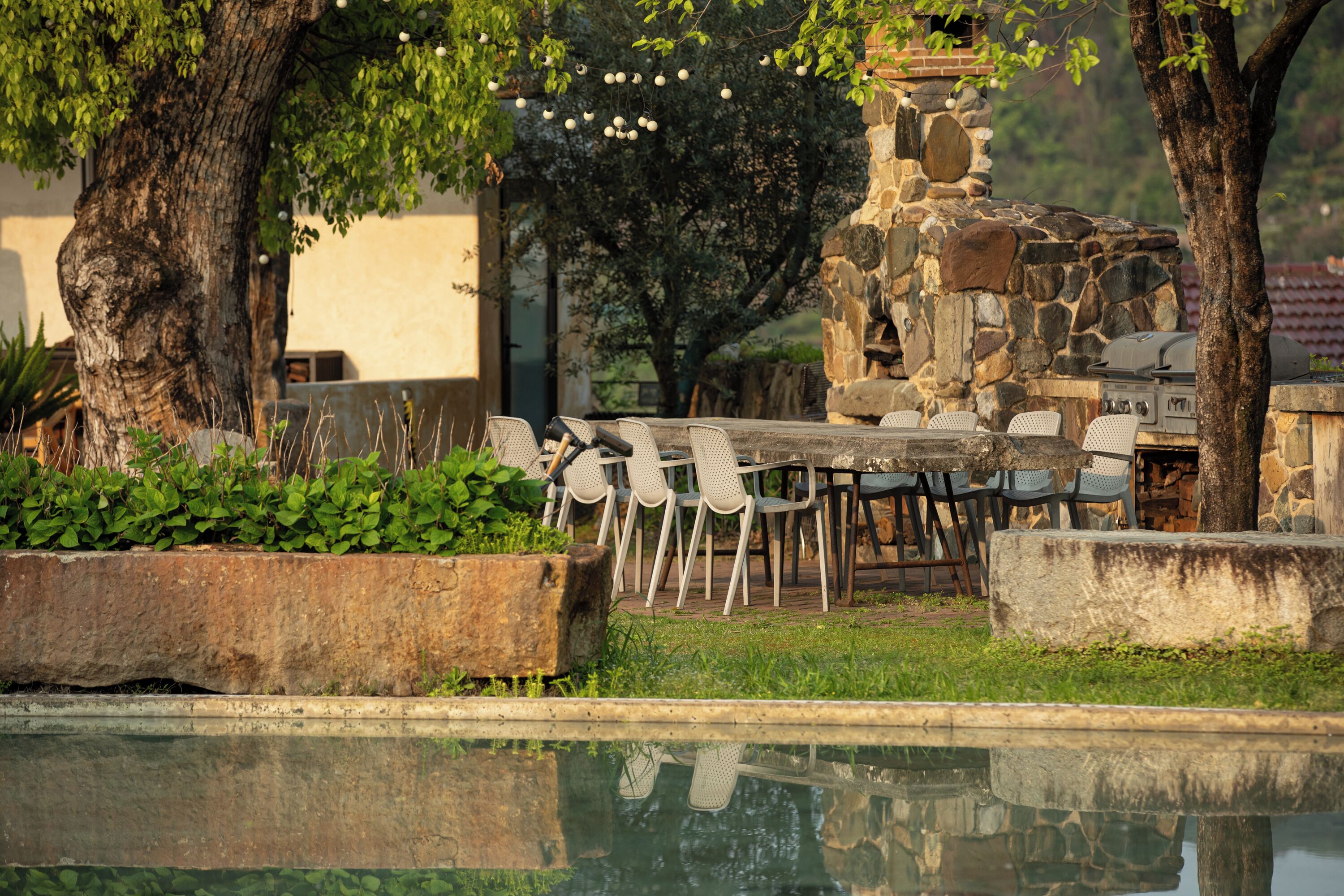 Zona de piscina con muro de piedra, mobiliario exterior y una parrilla.