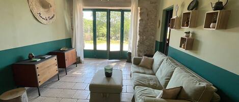 Ein Wohnzimmer mit Sofa, Couchtisch, Schrank, einem Hut an der Wand und Blick durch Glastüren.