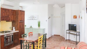A compact kitchen with wooden cabinets, a dining table with chairs, a TV on a stand, and a sofa in the living area. - La Casa di Pippo (Pollutri)