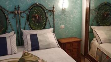 A bed with a floral-patterned pillow, a nightstand, a mirror, and a wall-mounted light fixture.