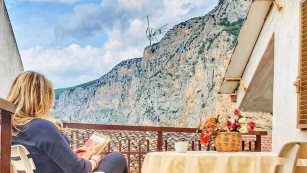 Una persona sentada a una mesa en un balcón con vistas a un acantilado rocoso.