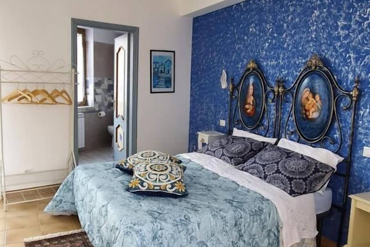 A bedroom with a bed, a blue wall, a door, and a hanging light fixture.
