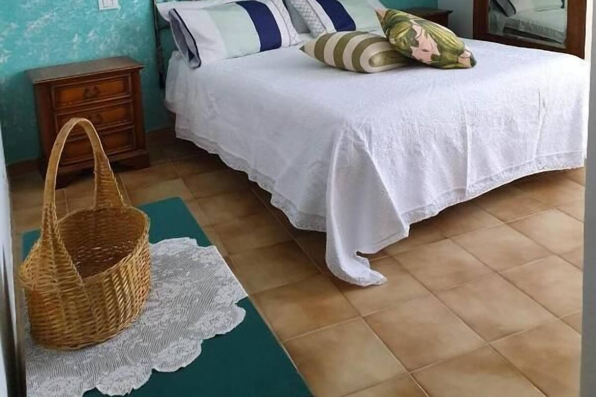 A bedroom with a bed, a nightstand, a wicker basket, and a mirror.