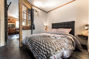 Un dormitorio con una cama grande, vigas de madera, una ventana con cortinas y vistas a la cocina.