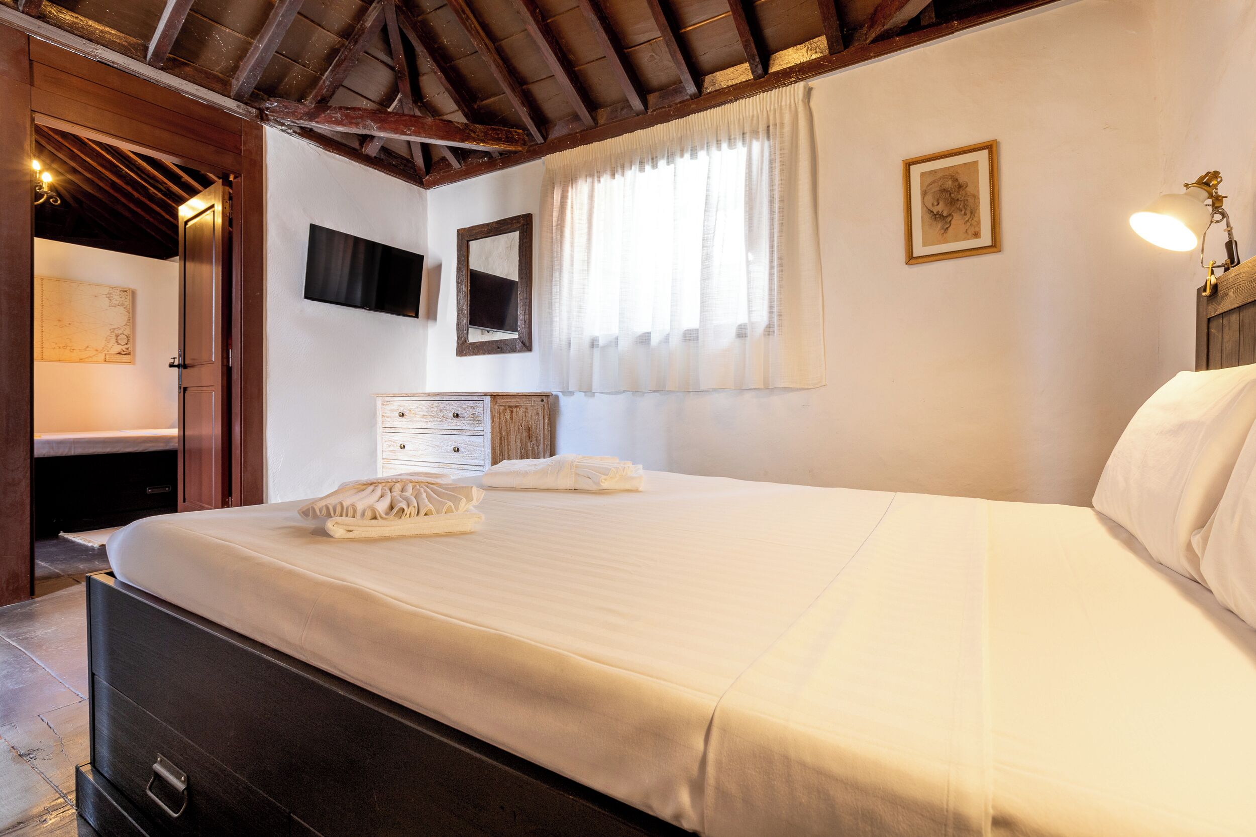 Un dormitorio con cama, cómoda, televisor y ventana con cortinas.