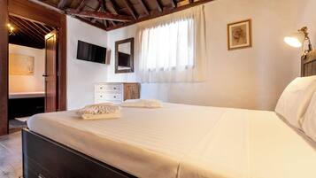 Un dormitorio con cama, cómoda, televisor y ventana con cortinas.