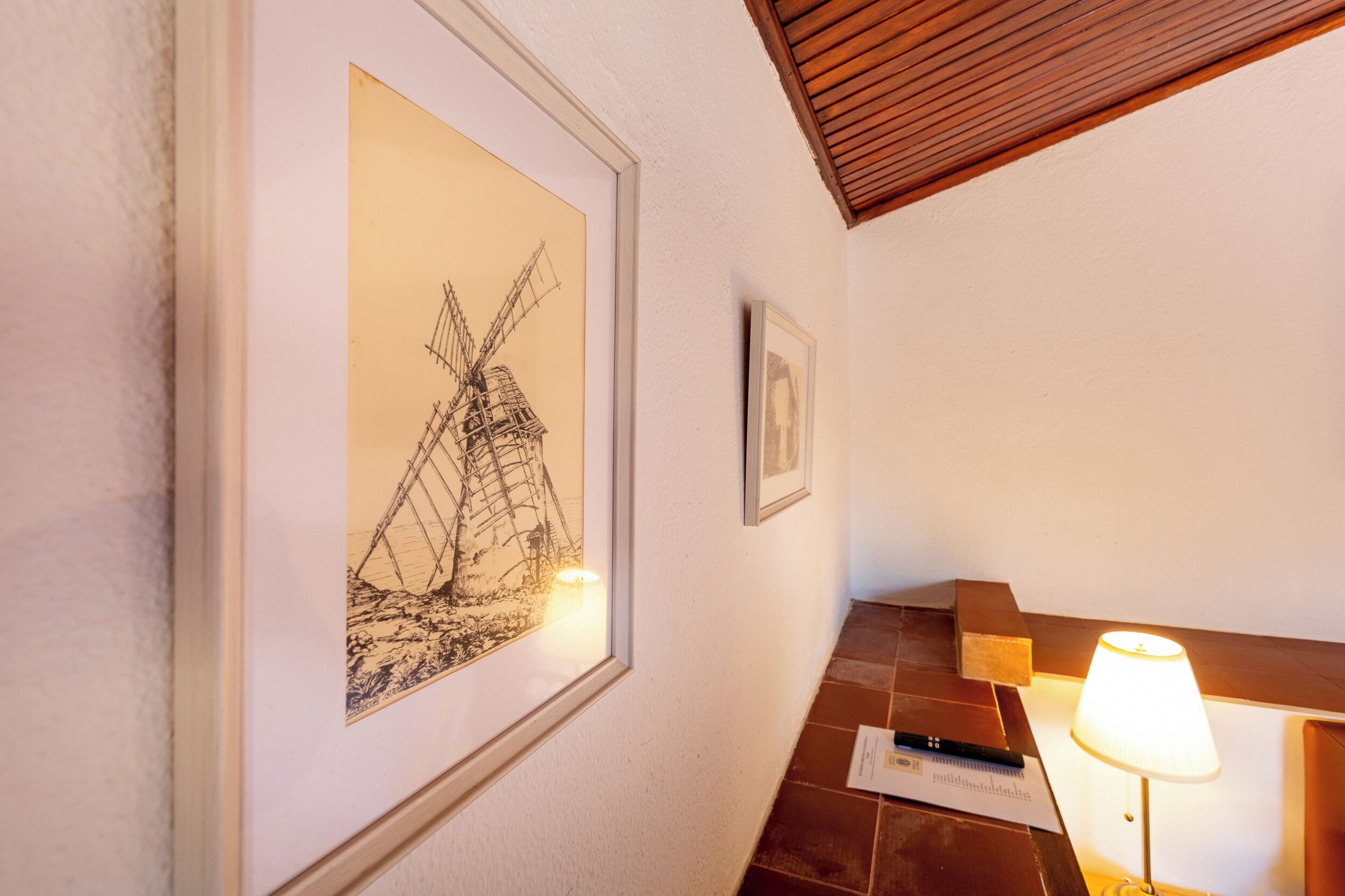 A framed windmill artwork, a small framed picture, a piano, and a lamp on a wall.