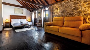 A room with a bed, a sofa, a stone wall, and wooden beams. - Hotel Emblemático Duque de la Torre (Arona)