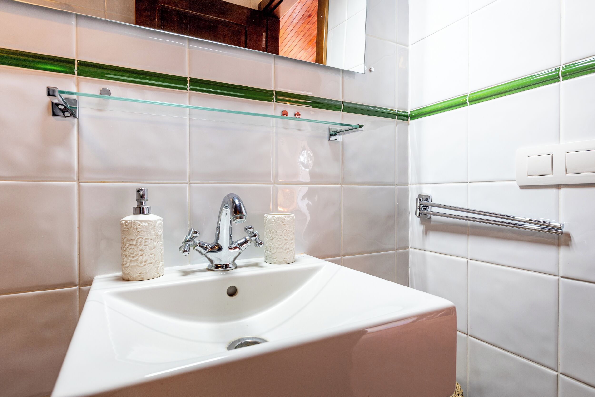 Un baño con un lavamanos blanco, dos rollos de papel higiénico, un grifo y un estante de vidrio sobre el lavamanos.