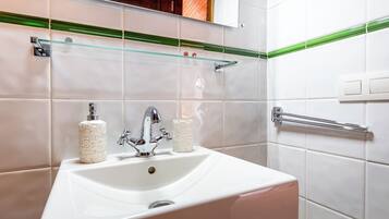 Un baño con un lavamanos blanco, dos rollos de papel higiénico, un grifo y un estante de vidrio sobre el lavamanos.