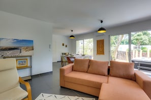 Un salon comprenant un canapé, un fauteuil, une table à manger avec des chaises et une grande fenêtre donnant sur un beau paysage.