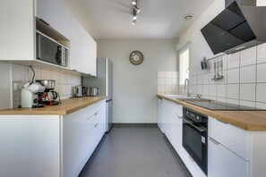 Une cuisine moderne avec des meubles blancs, un plan de travail en bois, un four encastré et une horloge murale.