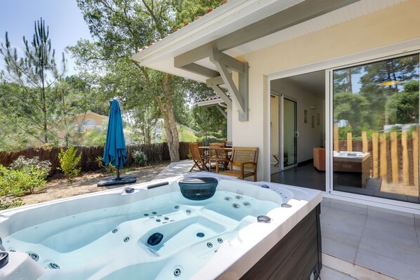 Un jacuzzi installé dans un jardin, avec une terrasse, du mobilier d’extérieur et une vue sur une maison.