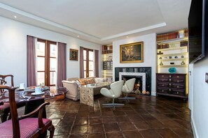A spacious living room with a fireplace, a dining area with a table and chairs, and a bookshelf filled with books and decorative items. - Stunning Palace With Terrace in C diz Center Calderon de la Barca (Cádiz)
