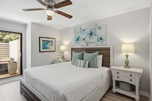 Ein Schlafzimmer mit einem Bett, zwei Nachttischen, einem Deckenventilator, Kunstwerken und Blick durch eine Glastür.