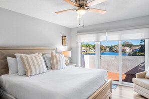 Ein Schlafzimmer mit Bett, Deckenventilator, Nachttisch mit Lampe und Blick auf einen Swimmingpool durch große Schiebeglastüren.
