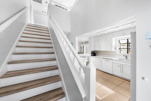 Eine Treppe mit Holzboden und weißen Geländern führt zu einer Küche mit weißen Schränken und einem Fenster.