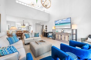 Ein geräumiges Wohnzimmer mit hoher Decke, einem großen Flachbildfernseher und Blick auf den Ozean.