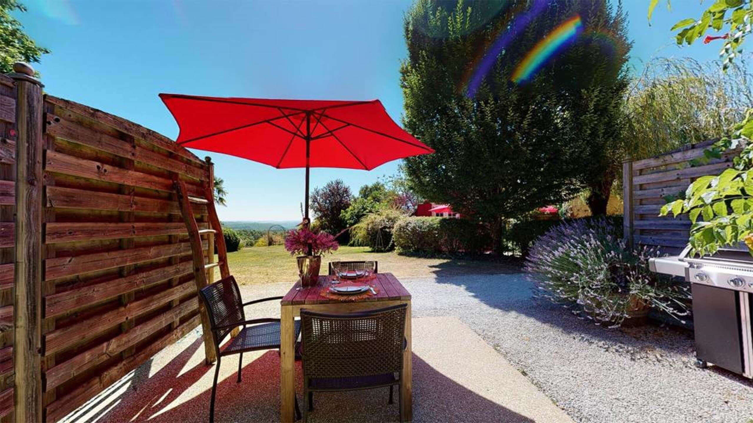 Een houten terras met een tafel, stoelen, een rode parasol en een barbecue.