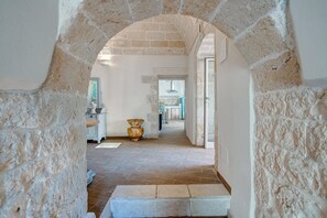 Un pasillo con paredes de piedra y suelo de baldosas, que conduce a una habitación con un lavabo y armarios.