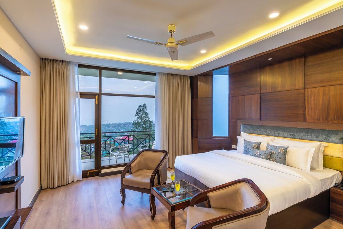 Quarto de hotel com cama, duas cadeiras, televisão e varanda com vista.