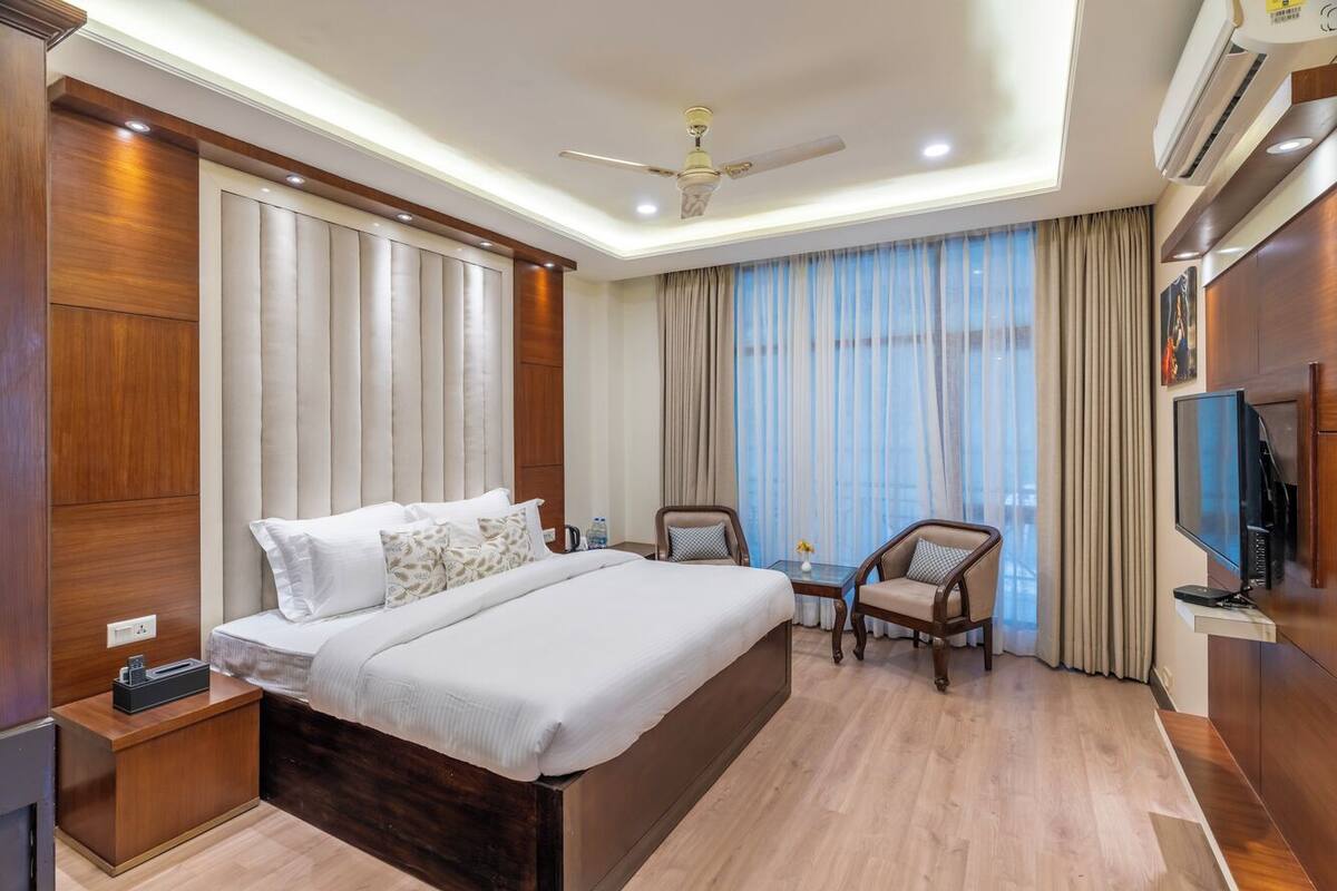 Quarto de hotel com uma cama grande, duas cadeiras, uma mesa pequena, uma televisão e um ar condicionado.