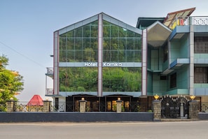 A modern hotel building with a glass facade, balconies, and a sign reading 'Hotel Karnika.' - Karnika Resort By White Panda Hotels (Dharamshala)