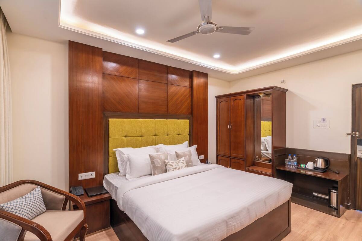 Quarto de hotel com cama, cabeceira de madeira, guarda-roupa, escrivaninha com espelho e ventoinha no teto.