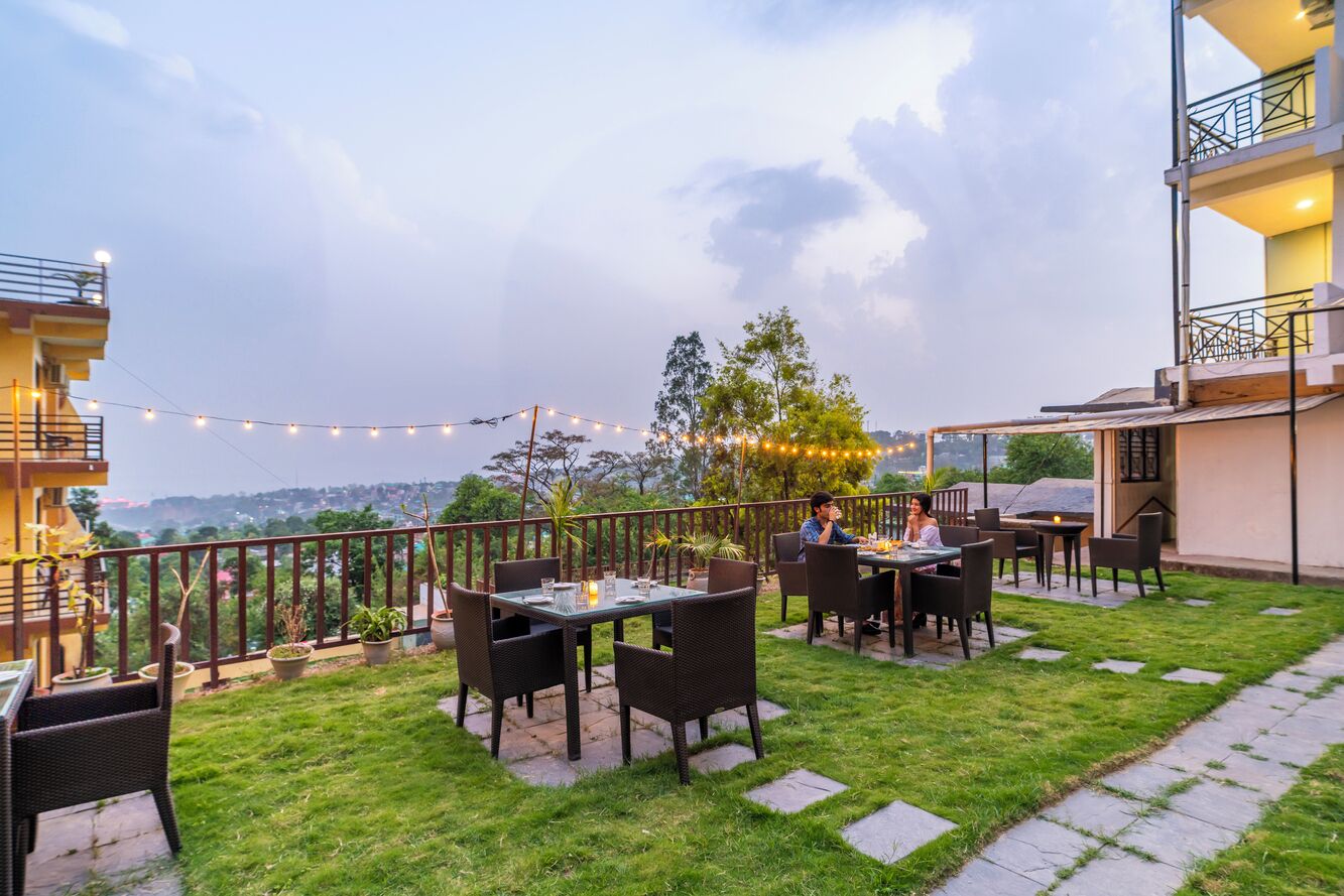 An outdoor patio with tables and chairs, a railing, and a view of the landscape.