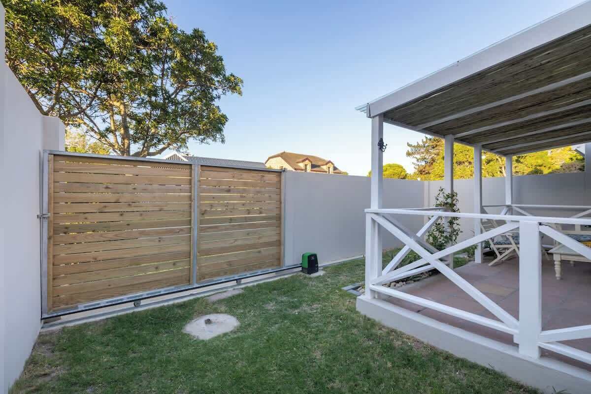 A backyard with a wooden fence, a white outdoor seating area, and a tree.