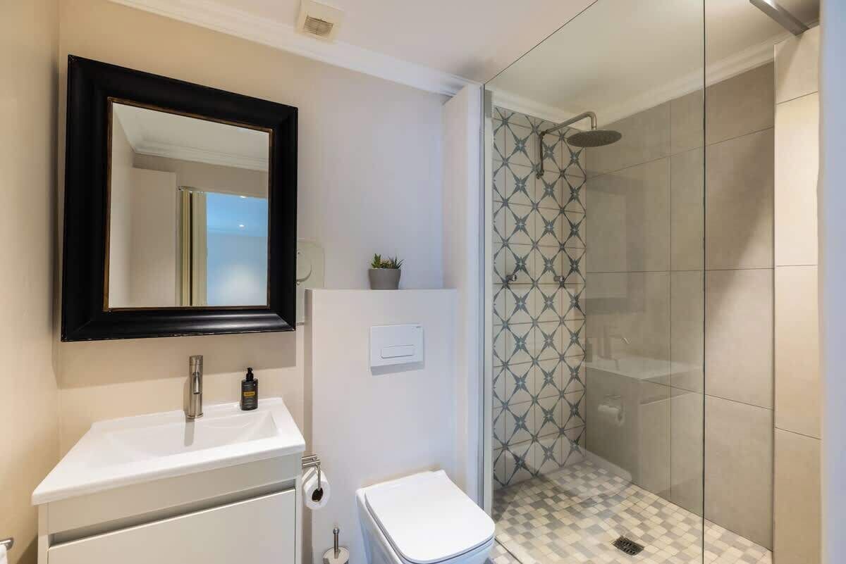 A bathroom with a white sink, a mirror, a toilet, and a shower with patterned tiles.