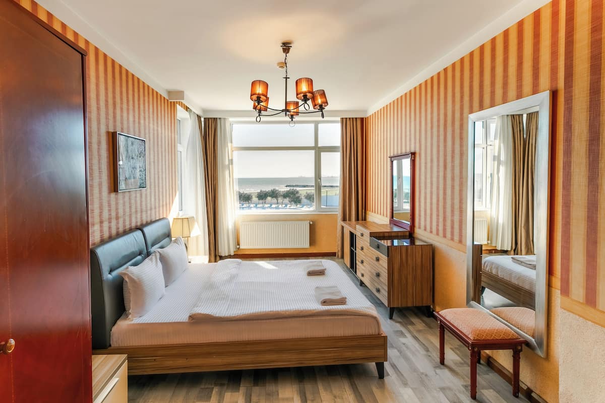 Habitación de hotel con una cama grande, un aparador, un banco, una araña y vistas al exterior.